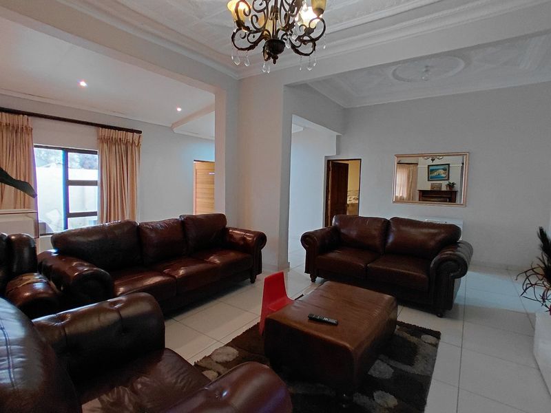 Spacious living room featuring tiled flooring, ornate ceiling detailing, and a central chandelier, offering a bright and open layout.