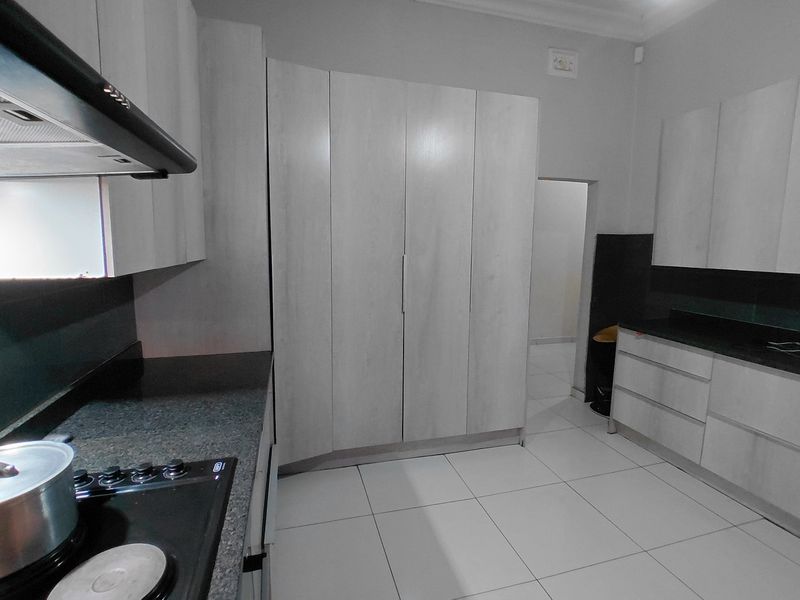 Modern kitchen featuring light wood-finish cabinetry, dark stone countertops, integrated hob with extractor fan, and clean white floor tiles.