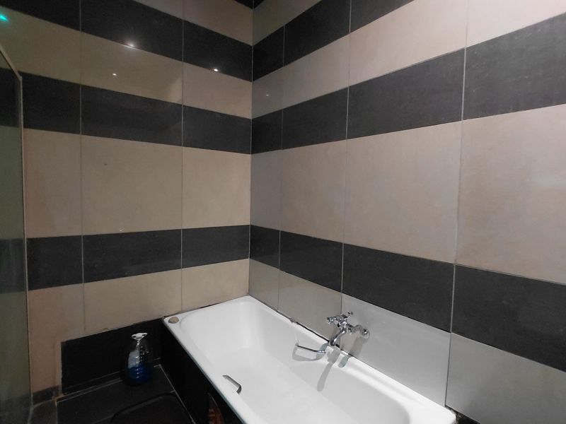 A bathroom featuring a built-in bathtub with chrome mixer tap and contrasting horizontal striped wall tiling.