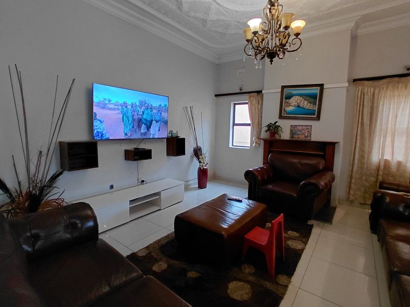 A spacious living room featuring an ornate ceiling rose, tiled flooring, and a traditional fireplace mantel, offering a comfortable and classic living space.
