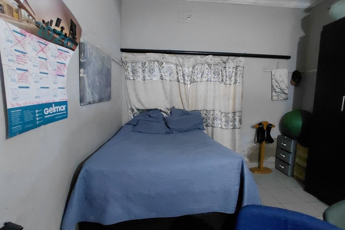 A bedroom featuring tiled flooring and a curtained window, showing visible signs of ceiling water damage.