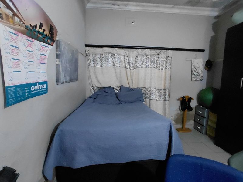 A bedroom featuring tiled flooring and a curtained window, showing visible signs of ceiling water damage.