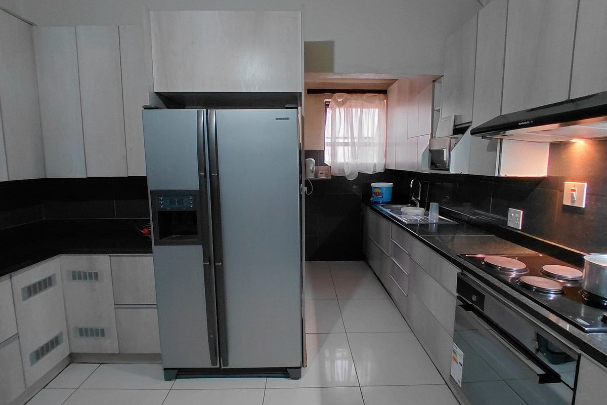 Modern kitchen featuring sleek cabinetry, granite countertops, integrated electric hob, oven, extractor fan, and tiled flooring with a functional layout.