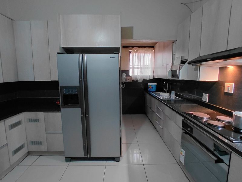 Modern kitchen featuring sleek cabinetry, granite countertops, integrated electric hob, oven, extractor fan, and tiled flooring with a functional layout.
