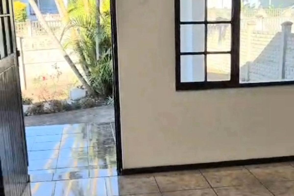 An empty living area featuring tiled flooring and large grid-pattern windows, providing direct access to an outdoor patio space.