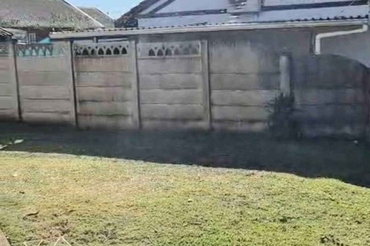 Rear exterior view of the property featuring a lawn, concrete pathway, and a precast concrete boundary wall with an external air conditioning unit.