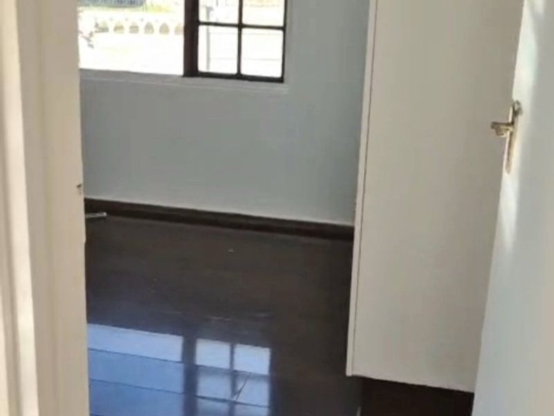An empty bedroom featuring dark laminate flooring, a grid-pattern window, and a built-in cupboard, offering a clean and neutral space.