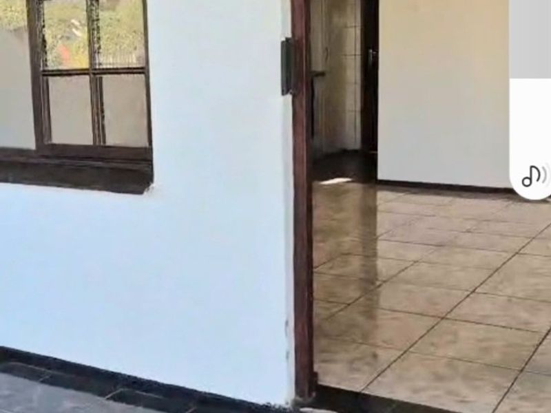 A view from a tiled patio looking into an empty interior space with tiled flooring and a wooden-framed window.