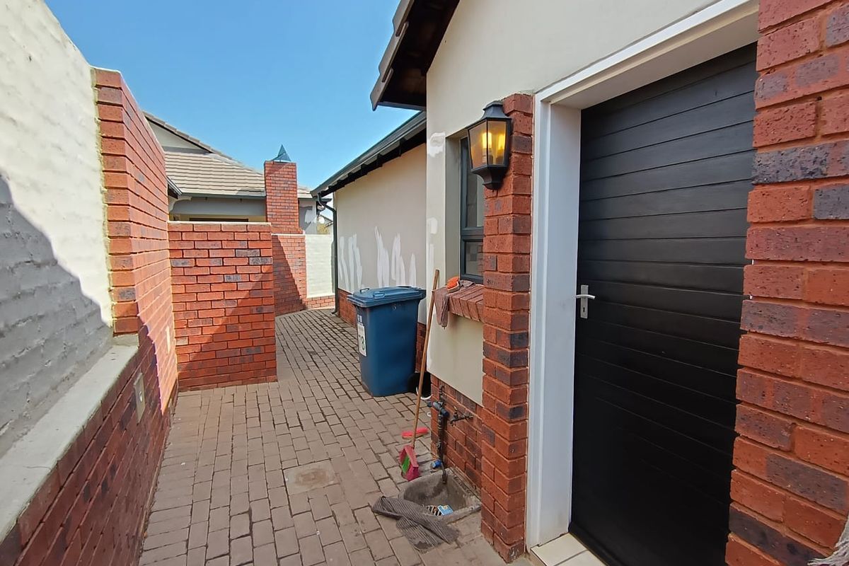 A side courtyard area featuring brick paving, a dark entrance door, and exterior wall lighting, with some visible paint touch-ups on the wall.