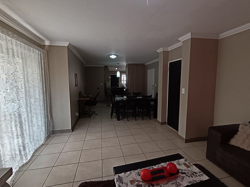 Spacious open-plan living and dining area featuring neutral wall tones, tiled flooring, crown molding, and a large sliding door providing natural light.