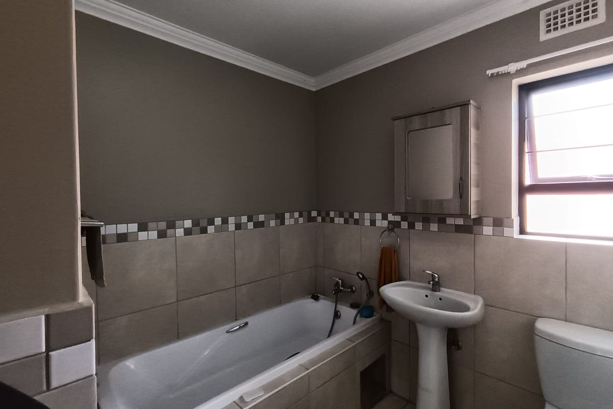 A functional bathroom featuring a pedestal basin, built-in bathtub, and wall-mounted medicine cabinet with neutral wall tones and tiled splashback detailing.