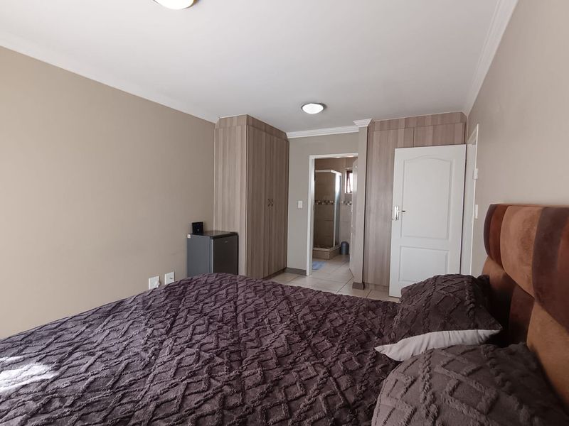 A well-maintained bedroom featuring built-in cupboards, neutral wall tones, and direct access to an en-suite bathroom.