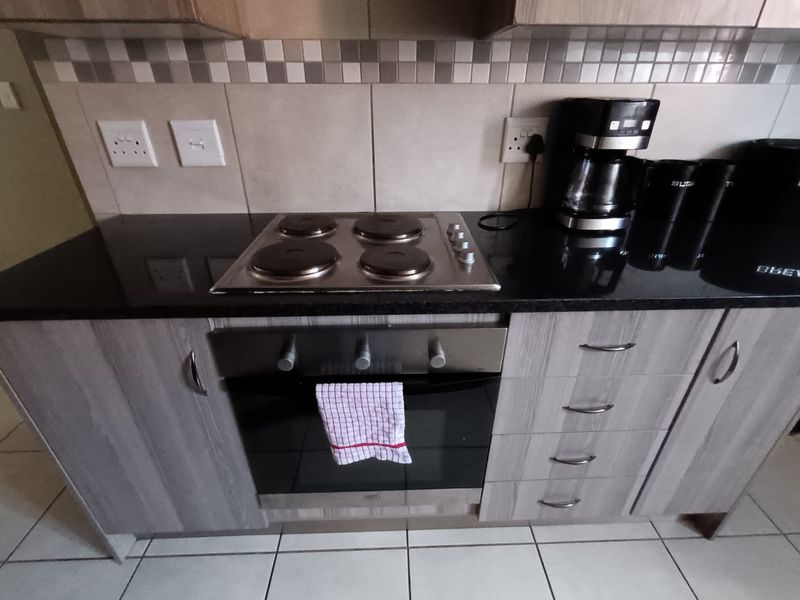 A functional kitchen area featuring a built-in oven, electric hob, granite countertops, and modern laminated cabinetry with a tiled backsplash.