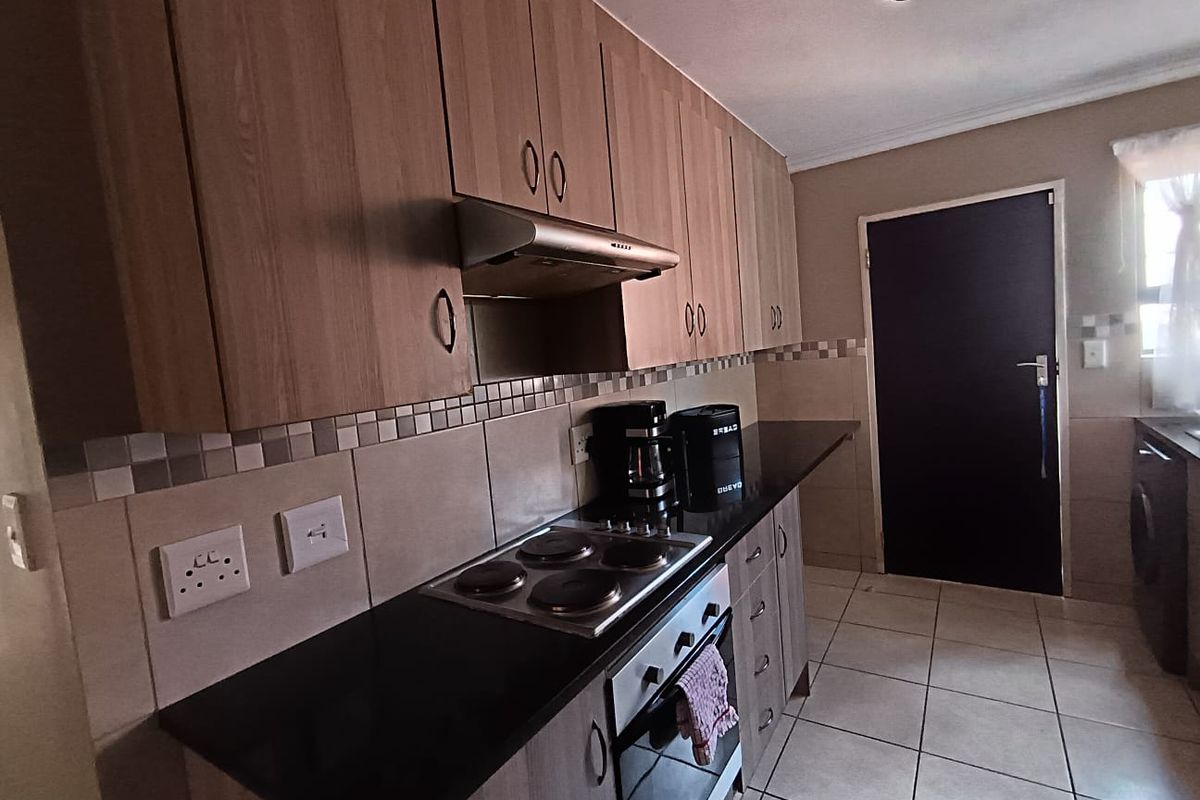 A functional kitchen featuring wood-look cabinetry, dark countertops, a built-in electric hob and oven, and tiled flooring with a neutral backsplash.