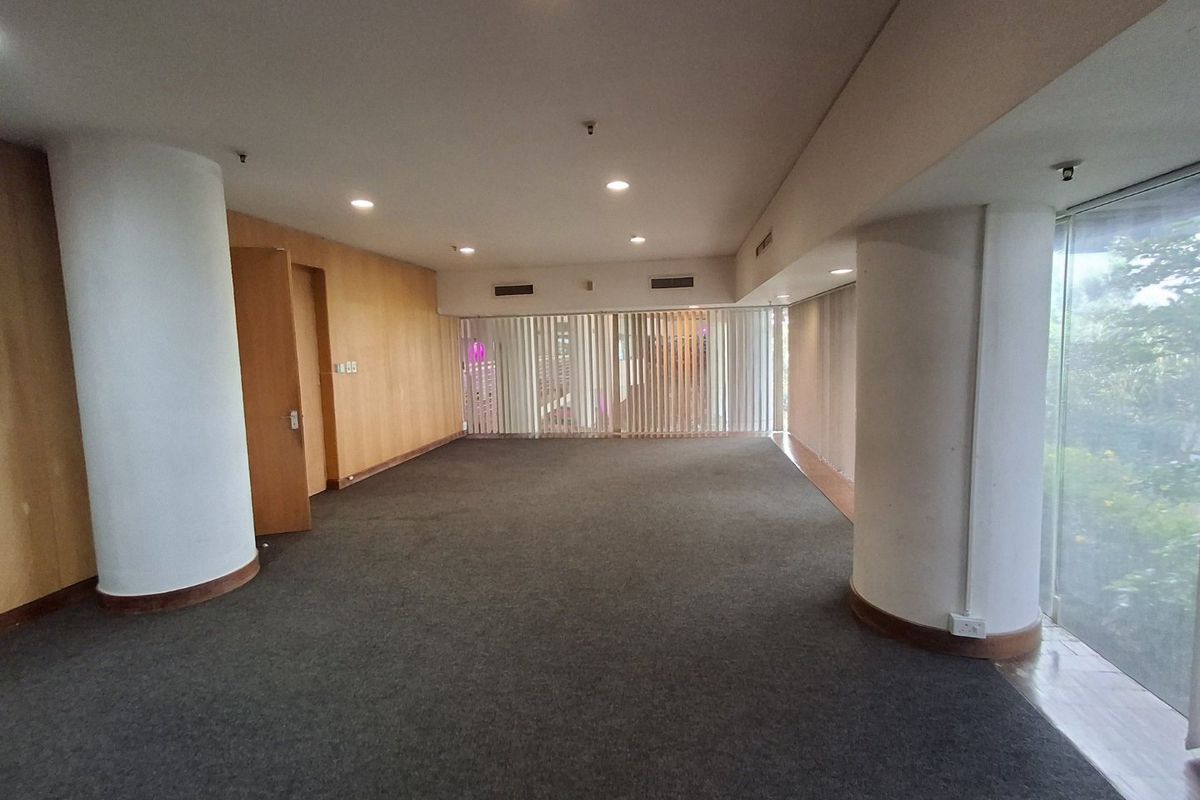 Spacious open-plan commercial office area featuring wood veneer wall paneling, large floor-to-ceiling windows with vertical blinds, and recessed ceiling lighting.