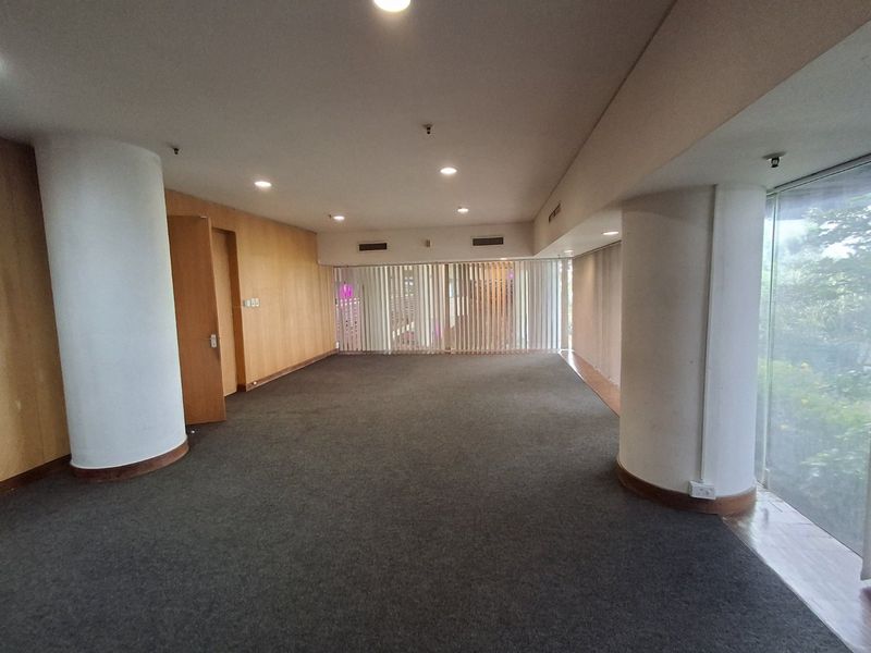 Spacious open-plan commercial office area featuring wood veneer wall paneling, large floor-to-ceiling windows with vertical blinds, and recessed ceiling lighting.