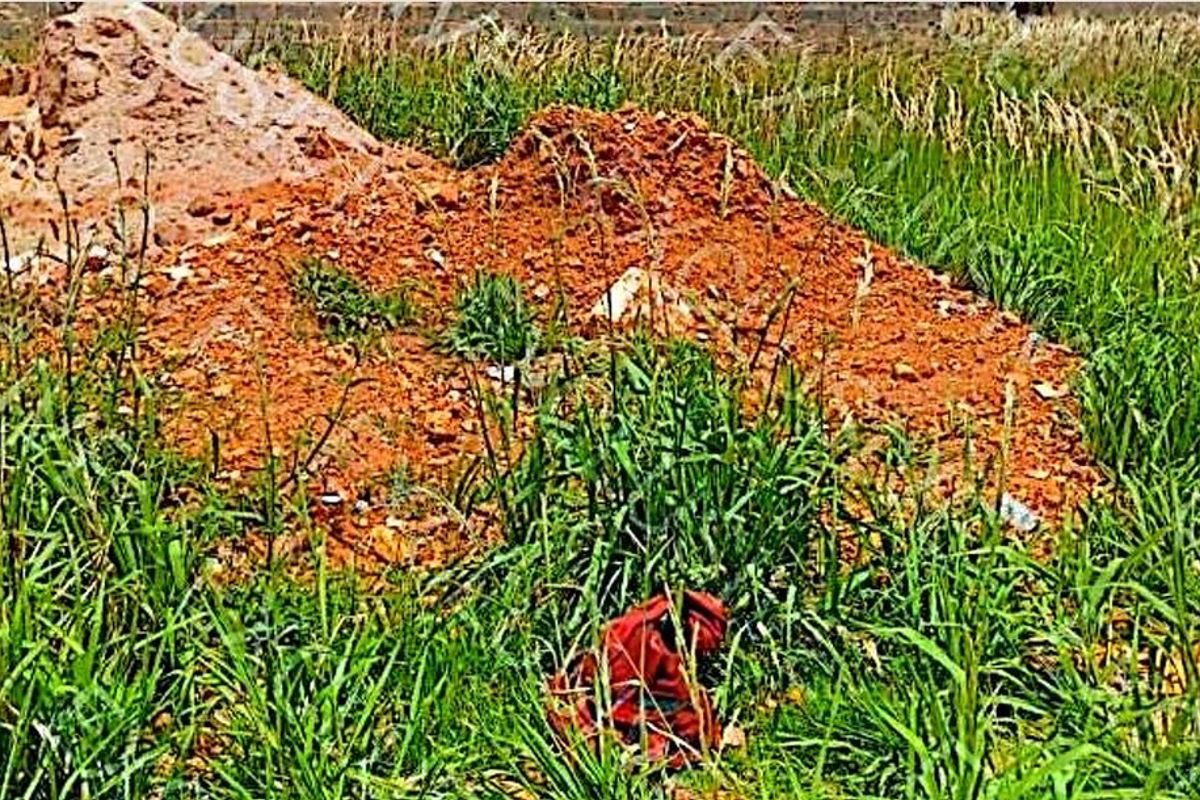 A view of an undeveloped residential plot featuring overgrown grass and piles of excavated soil.
