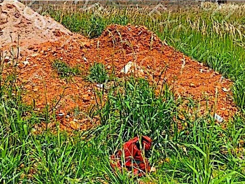 A view of an undeveloped residential plot featuring overgrown grass and piles of excavated soil.