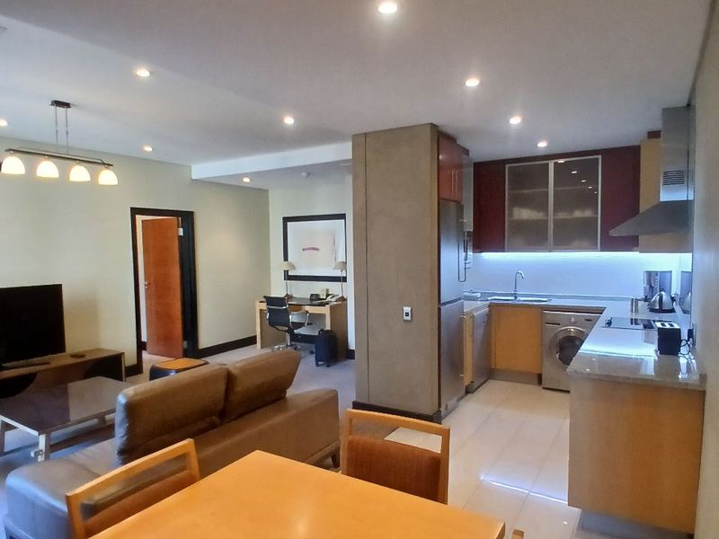Open-plan living area featuring a modern kitchen with built-in cabinetry, integrated appliances, and a dedicated workspace, finished with tiled flooring and recessed lighting.