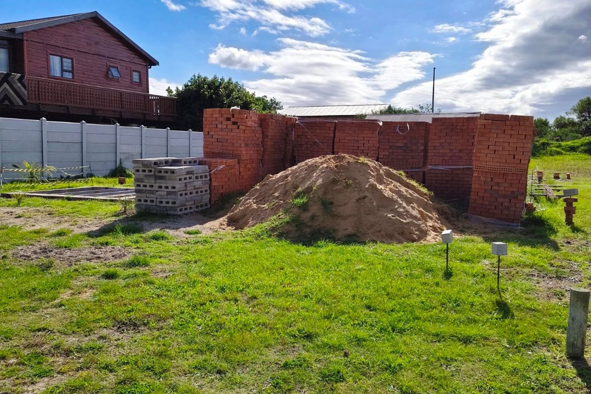 Vacant residential land featuring a precast boundary wall, stacked construction materials, and a pile of sand, ready for development.
