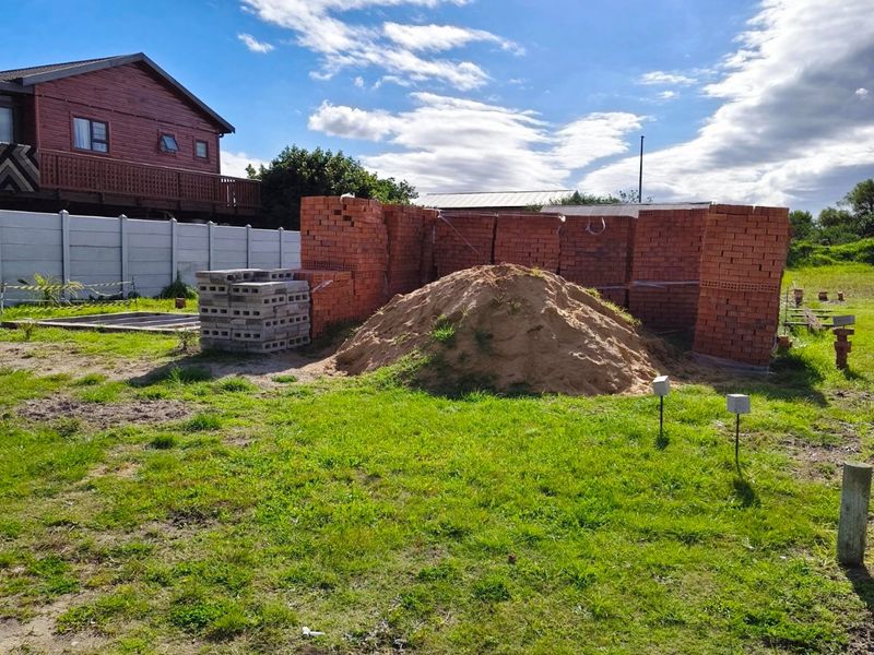 Vacant residential land featuring a precast boundary wall, stacked construction materials, and a pile of sand, ready for development.