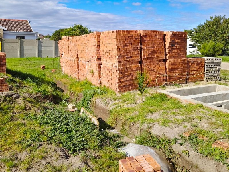 Vacant residential land featuring a concrete foundation and stacks of construction bricks, indicating ongoing site preparation or building works.