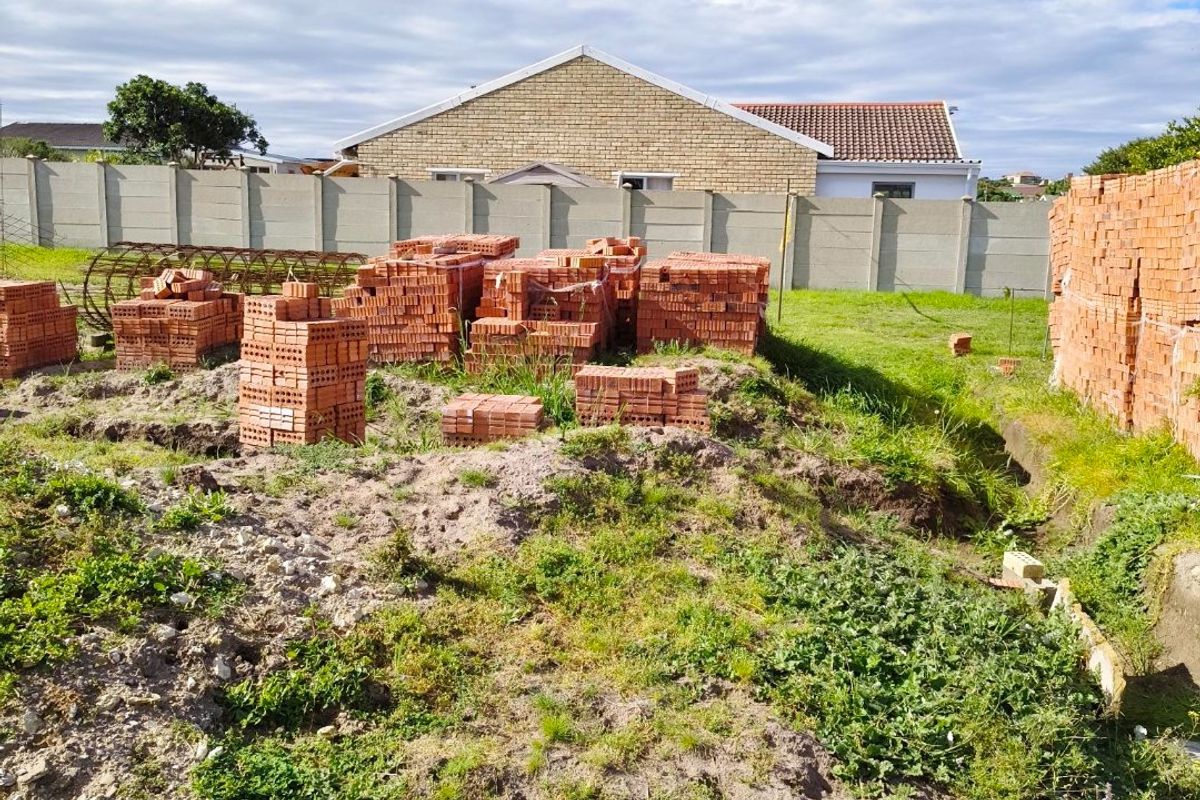 A vacant residential plot featuring excavated ground and stacked construction bricks, enclosed by a precast concrete boundary wall.