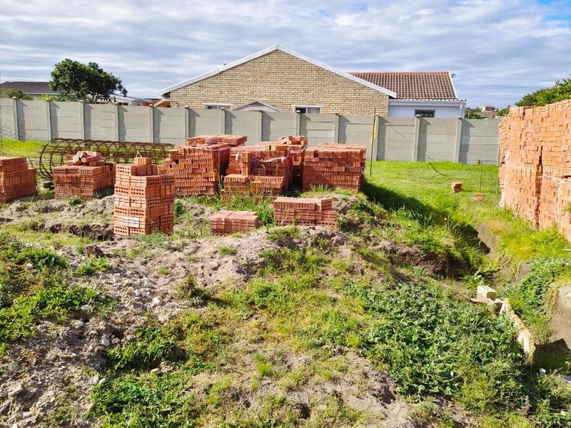 A vacant residential plot featuring excavated ground and stacked construction bricks, enclosed by a precast concrete boundary wall.