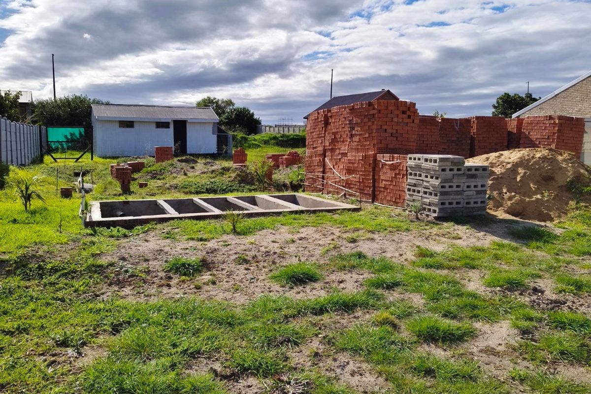 Vacant residential plot featuring a concrete foundation, an existing outbuilding, and stored construction materials on site.