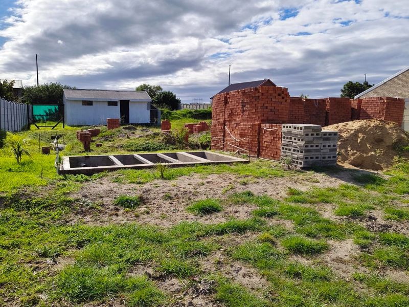 Vacant residential plot featuring a concrete foundation, an existing outbuilding, and stored construction materials on site.