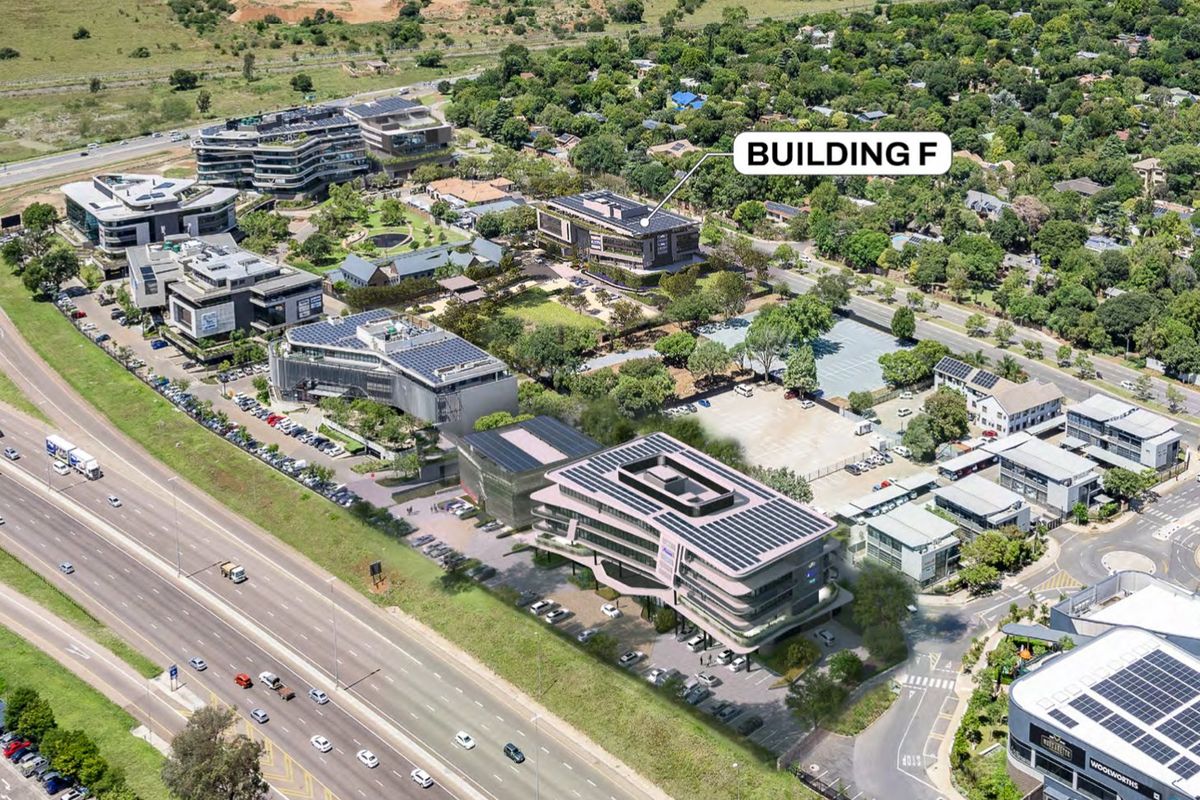 Aerial view of a commercial office park featuring multiple buildings, extensive parking facilities, and landscaped green spaces with solar panel installations.