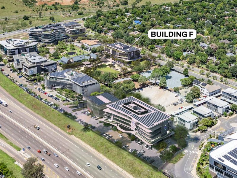 Aerial view of a commercial office park featuring multiple buildings, extensive parking facilities, and landscaped green spaces with solar panel installations.