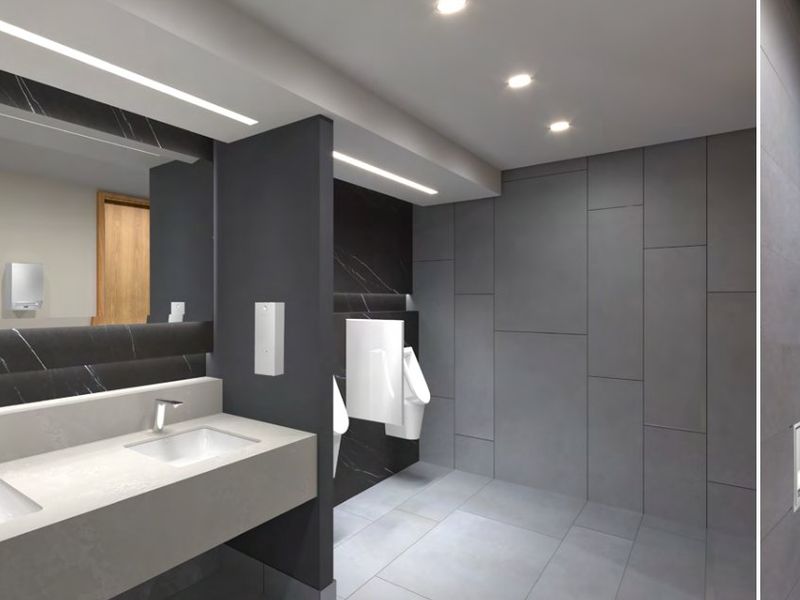 Modern commercial bathroom featuring a double vanity with integrated sinks, wall-hung toilet, urinals, and high-end dark marble-effect and grey tile finishes.