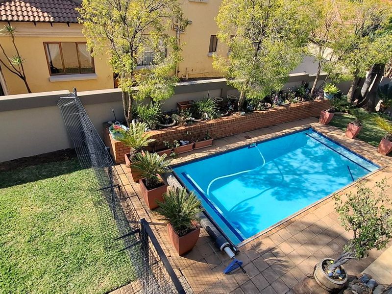 An elevated view of a private backyard featuring a swimming pool, paved patio area, landscaped garden beds, and a well-maintained lawn.