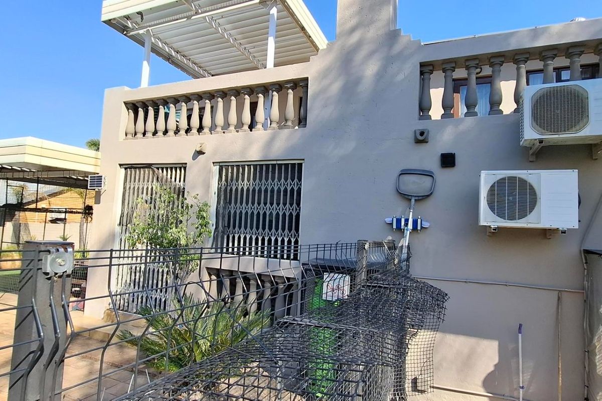Rear exterior view of the property featuring a balcony with balustrades, pergola, security gates, and wall-mounted air conditioning units overlooking the pool area.
