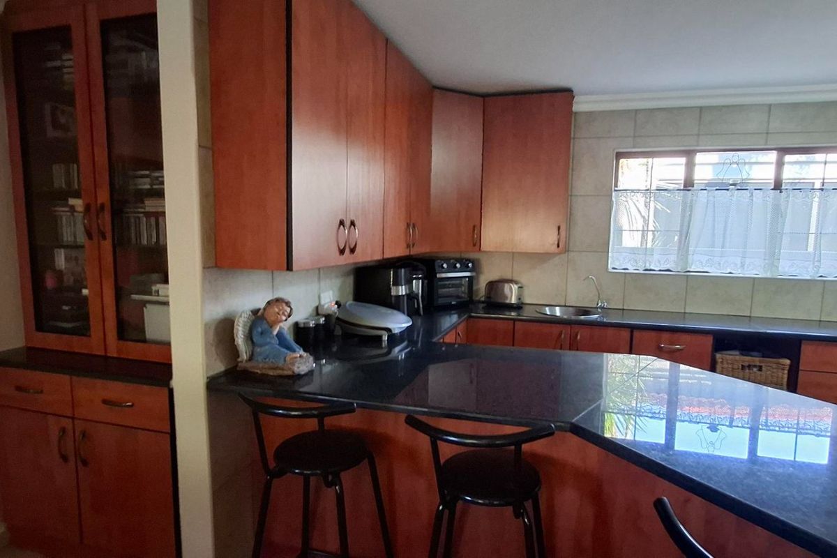 A functional kitchen featuring warm-toned wooden cabinetry, dark granite countertops, a breakfast bar, and a tiled backsplash with a window for natural light.