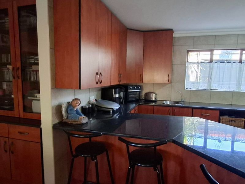 A functional kitchen featuring warm-toned wooden cabinetry, dark granite countertops, a breakfast bar, and a tiled backsplash with a window for natural light.