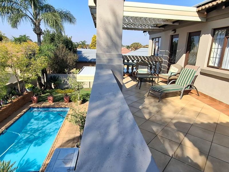 A spacious covered patio featuring tiled flooring and a pergola, overlooking a private swimming pool and landscaped garden area.