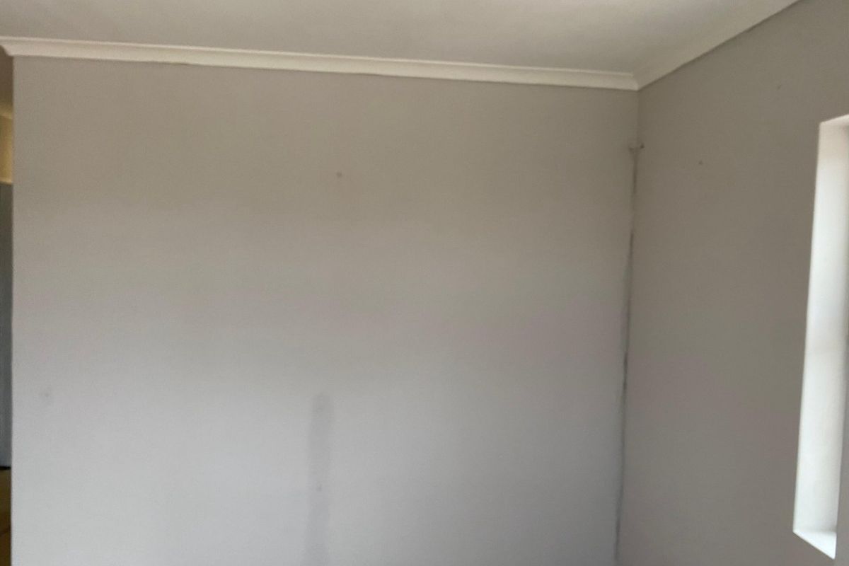 An empty bedroom featuring neutral painted walls, cornice detailing, and visible wall cracking requiring maintenance.