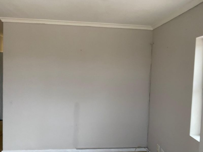 An empty bedroom featuring neutral painted walls, cornice detailing, and visible wall cracking requiring maintenance.