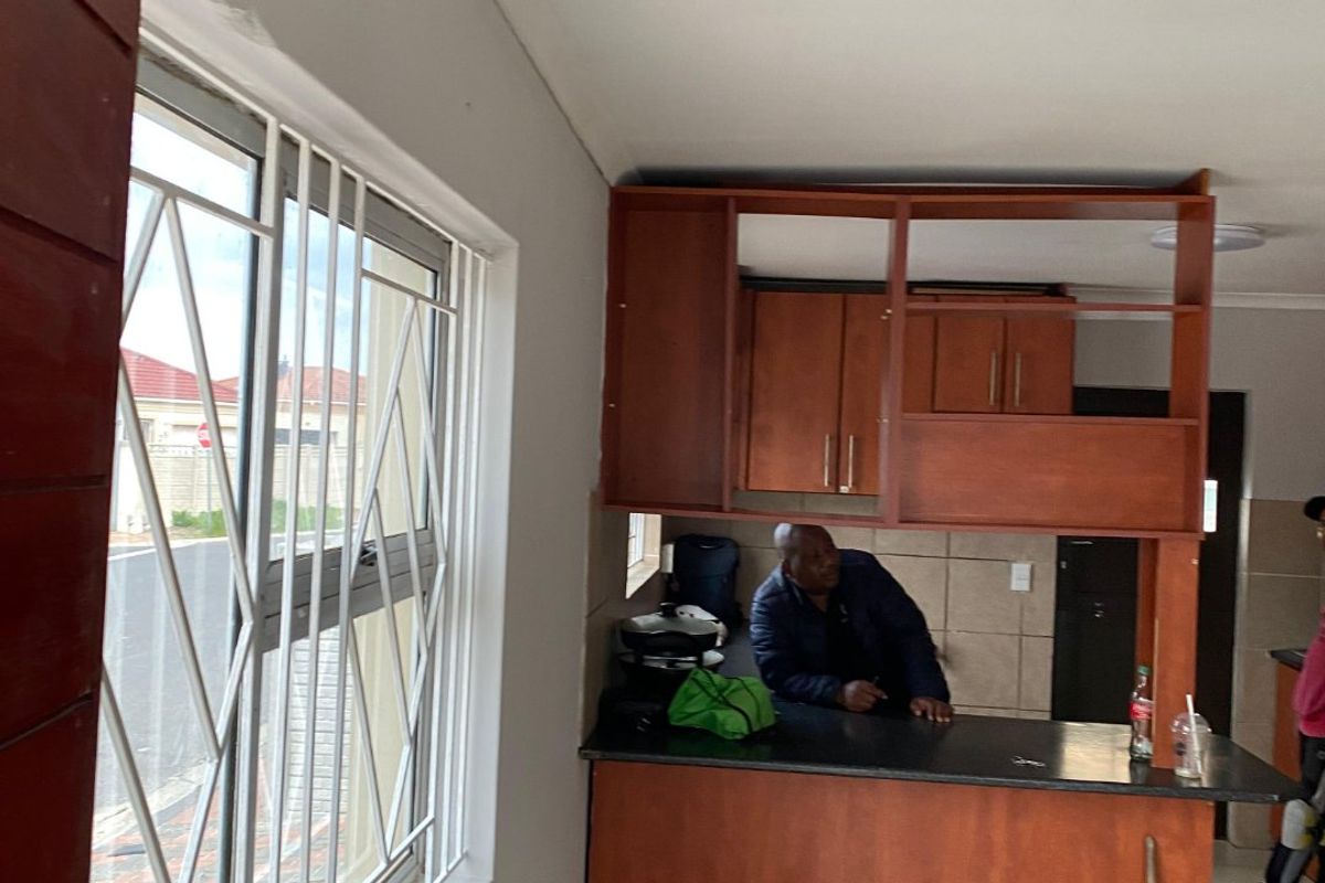 A kitchen area featuring wooden cabinetry, a breakfast bar, and tiled splashbacks, with security bars installed on the window.