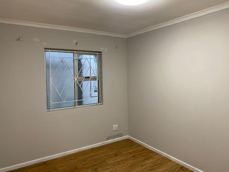 An empty bedroom featuring laminate flooring, security bars on the window, and visible wall surface imperfections requiring minor repair.