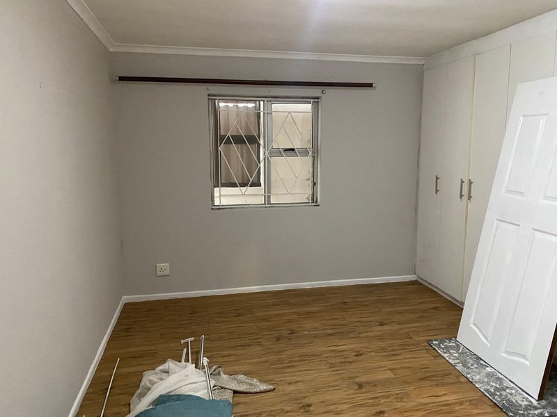 A vacant bedroom featuring laminate flooring, built-in cupboards, and a window with security bars, presenting a clean canvas for potential buyers.