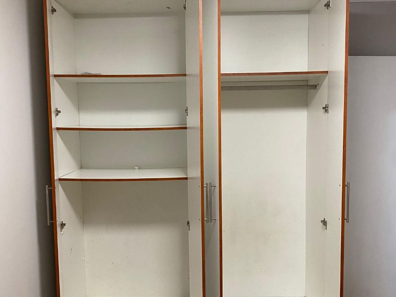 A bedroom featuring a built-in wardrobe with open shelving and hanging space, finished with laminate flooring.