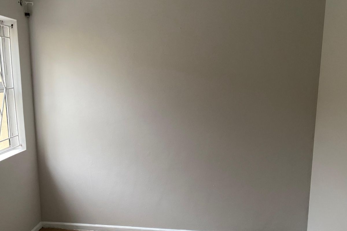 An empty bedroom featuring neutral painted walls, tiled flooring, and a window fitted with security bars.