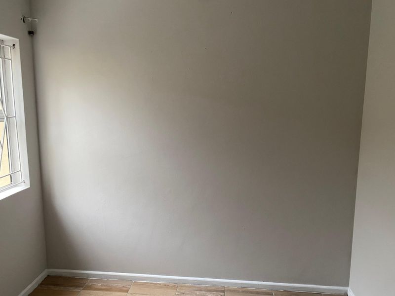 An empty bedroom featuring neutral painted walls, tiled flooring, and a window fitted with security bars.