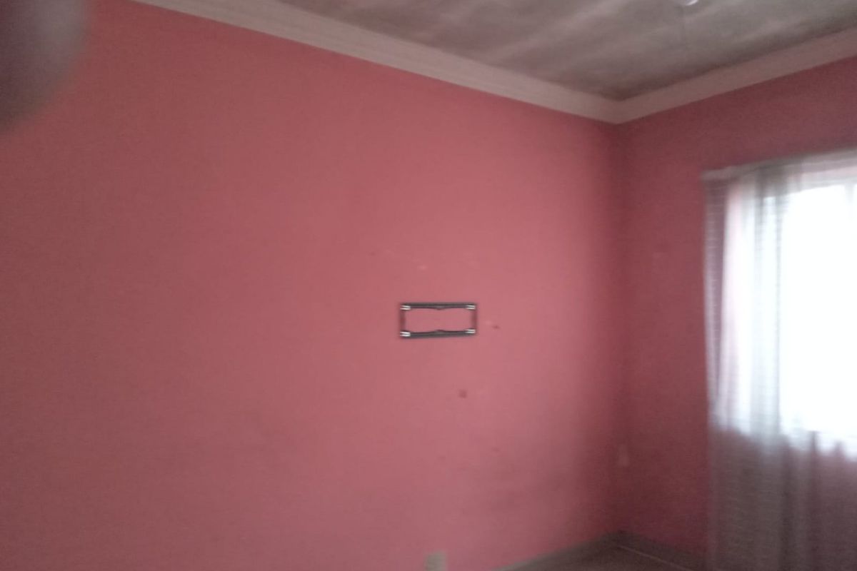 An empty bedroom featuring pink walls, crown molding, and a wall-mounted TV bracket, requiring cosmetic updates to improve its overall condition.