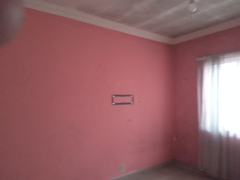 An empty bedroom featuring pink walls, crown molding, and a wall-mounted TV bracket, requiring cosmetic updates to improve its overall condition.
