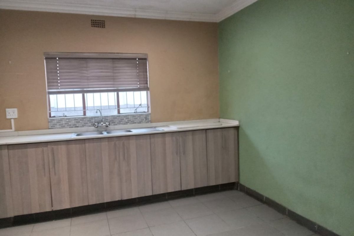 A functional kitchen area featuring built-in cabinetry, a stainless steel sink, tiled flooring, and a window with fitted blinds.