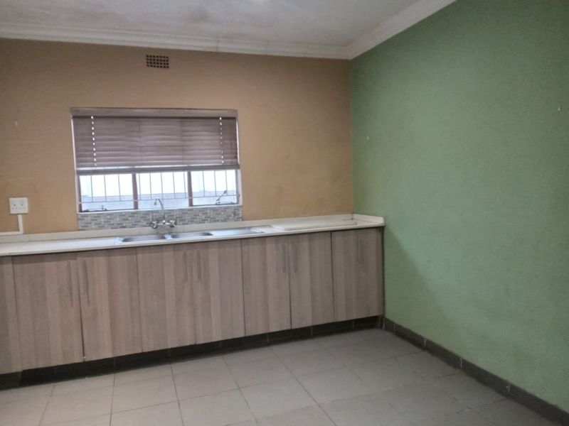 A functional kitchen area featuring built-in cabinetry, a stainless steel sink, tiled flooring, and a window with fitted blinds.